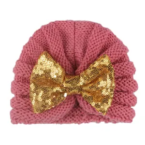 Texture de tricot détaillée et grand nœud à paillettes dorées sur bonnet rose bébé