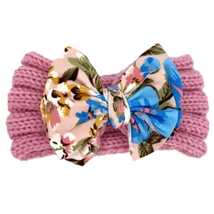 Détail d'un bandeau en tricot rose pour bébé avec un grand nœud en tissu fleuri vintage