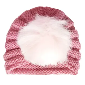 Dettaglio di un cappello in maglia rosa per neonati con trama a coste e grande pompon di pelliccia