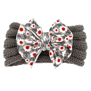 Détail d'un bandeau en maille pour bébé avec un grand nœud floral sur tissu gris foncé