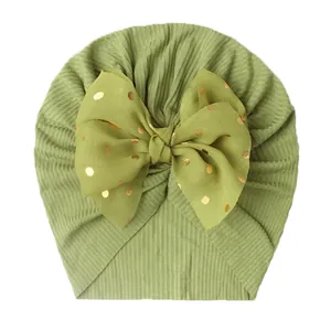 Detail of moss green ribbed knit baby turban featuring a large gold polka dot bow