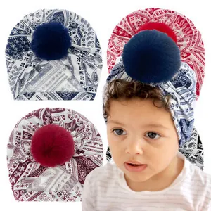 Detail of floral paisley baby turban with soft fabric and fluffy faux fur pom-poms