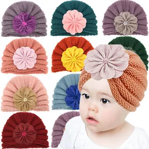 Close-up of soft knitted baby turban hats featuring large 3D floral accents in multiple colors