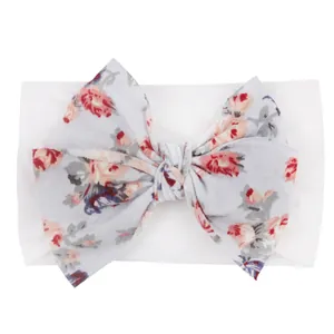Détail d'un bandeau en nylon pour bébé avec un grand nœud à imprimé rose sur tissu blanc