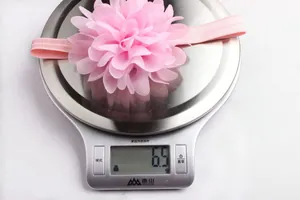 Fascia per neonati con fiore in chiffon rosa su bilancia che indica un peso di 6,5g
