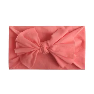 Detailopname van zachte koraalroze nylon hoofdband met een grote strik voor baby's
