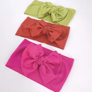 Close-up of three ribbed knit baby headbands in green, red, and pink with large bows