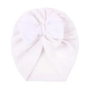 Détail d'un bonnet turban blanc pour bébé en velours avec un grand nœud décoratif