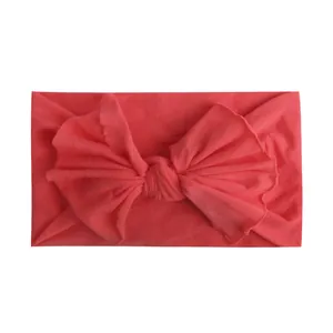 Detail van koraalroze nylon baby hoofdband met grote strik en zachte elastische stoftextuur