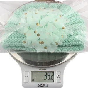 Detailansicht einer hellgrünen Baby-Strickmütze mit goldgepunkteter Mesh-Blume als Deko