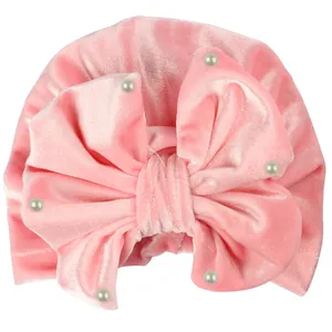 Pink velvet baby turban hat featuring a large soft bow with elegant white pearl accents
