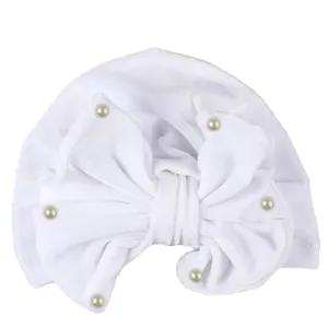 Detail of white velvet baby turban hat featuring large bow and pearl embellishments