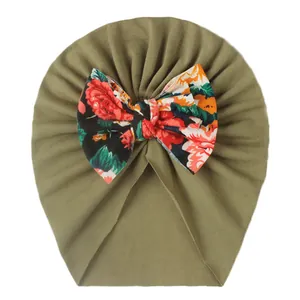 Nahaufnahme einer olivgrünen Babyhaube mit einer Blumen-Schleife und roten Rosen