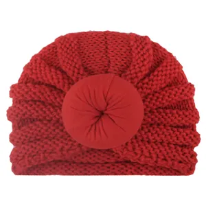 Dettaglio cappello neonato rosso a maglia con nodo a ciambella e trama a spirale