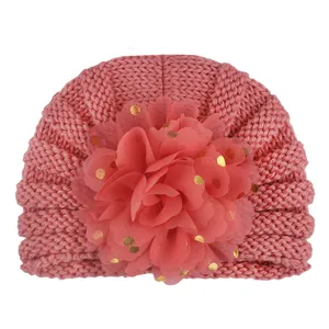 Nahaufnahme von Strickstruktur und Netzblume mit Goldpunkten auf rosa Babymütze