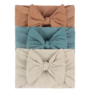 Detail of 3-pack nylon baby headbands with large bows in tan, grey-blue, and cream colors