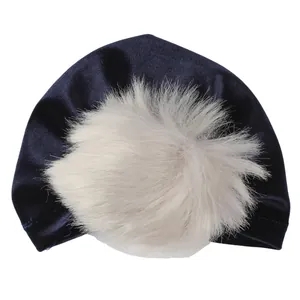 Dettaglio cappello invernale neonato in velluto blu scuro con grande pompon grigio decorativo