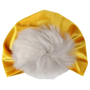 Dettaglio del caldo cappello turban per neonati in velluto dorato con pompon di pelliccia