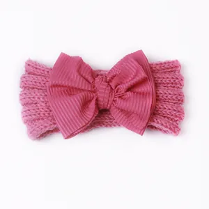 Detail eines rosa gestrickten Baby-Stirnbands mit großer Rippband-Schleife vor weißem Grund