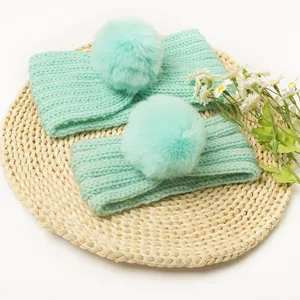 Detailed close-up of mint green knitted headbands with fur pompom on woven mat