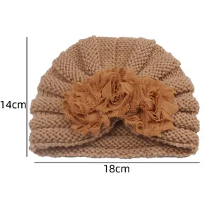 Detailed knit texture and dimensions of baby hat with decorative fabric flowers