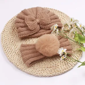 Close-up of knit baby turban with bow and matching faux fur pom pom headband in camel