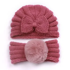 Close-up of pink knitted baby hat with bow and matching headband with faux fur pompom