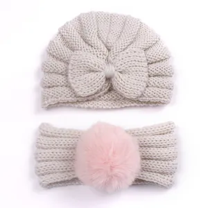 Detail of knitted baby hat with bow and headband featuring a pink faux fur pom-pom