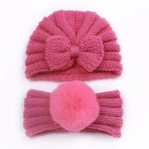 Detail of bright pink knitted baby hat with bow and headband with large pom-pom