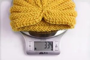 Detailed view of yellow knitted baby headband weighing 33.4g on a digital scale