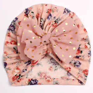 Detailed close-up of baby turban hat with floral print and large gold polka dot bow