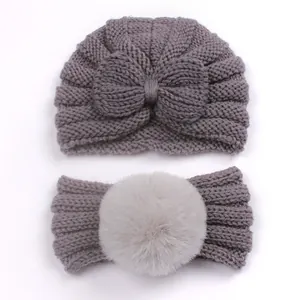 Detail view of grey knit baby turban hat with bow and matching faux fur pompom headband