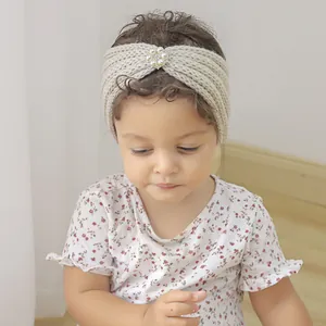 Detail of baby knitted headband with pearl rhinestone flower on cream crochet fabric