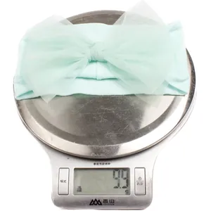 Detail showing the lightweight 9.9g mint green mesh bow headband on a scale