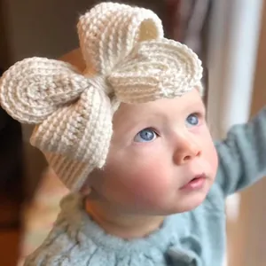 Gros plan d'un bandeau pour bébé tricoté avec un grand nœud crème sur une bande douce