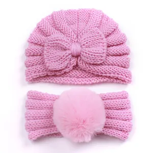 Detailed view of pink knitted baby hat with bow and matching faux fur pompom headband