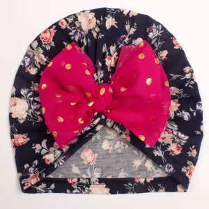 Close-up of baby floral turban hat with fuchsia chiffon bow and gold polka dots