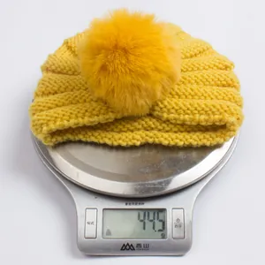 Détail d'un bonnet en tricot jaune avec pompon sur une balance pesant 44,5 grammes