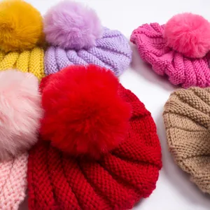 Vue détaillée de bonnets tricotés multicolores pour bébé avec de gros pompons en fourrure