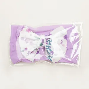 Detail of purple baby headband with white floral bow in individual protective packaging