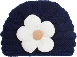 Dettaglio di un berretto in maglia blu scuro per neonati con un fiore bianco e bottone in legno