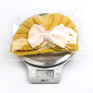 Winter baby knit hat with pink bow and pearls on a kitchen scale weighing 49.7g