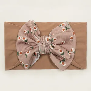 Detail of baby headband with tan elastic base and purple floral daisy bow ornament