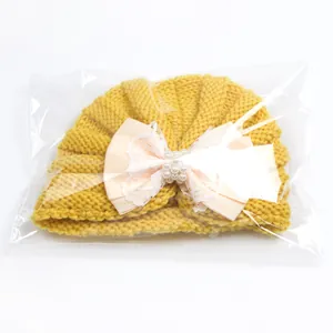 Detail of yellow baby knit turban hat featuring a lace pink bow with pearl accents