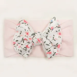 Detail of baby headband with a large pink floral bow on a soft ribbed knit strap