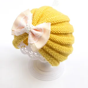 Detail of baby turban hat featuring a cream bow, lace layers, and pearl decorations