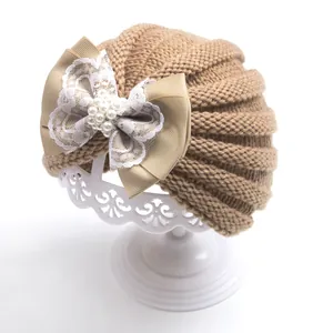 Detailed texture of camel baby turban hat with lace pearl bow on a white display stand