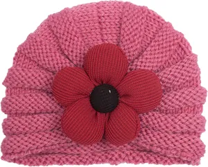 Dettaglio del cappello a turbante in maglia rosa per neonati con un fiore in tessuto rosso
