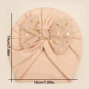 Flat lay detail of baby turban hat with gold polka dot bow and size 18x19 cm markings