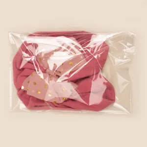 Pink winter baby turban hat with gold polka dot bow detail in clear packaging
